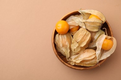 Ripe physalis fruits with calyxes in bowl on beige background, top view. Space for text