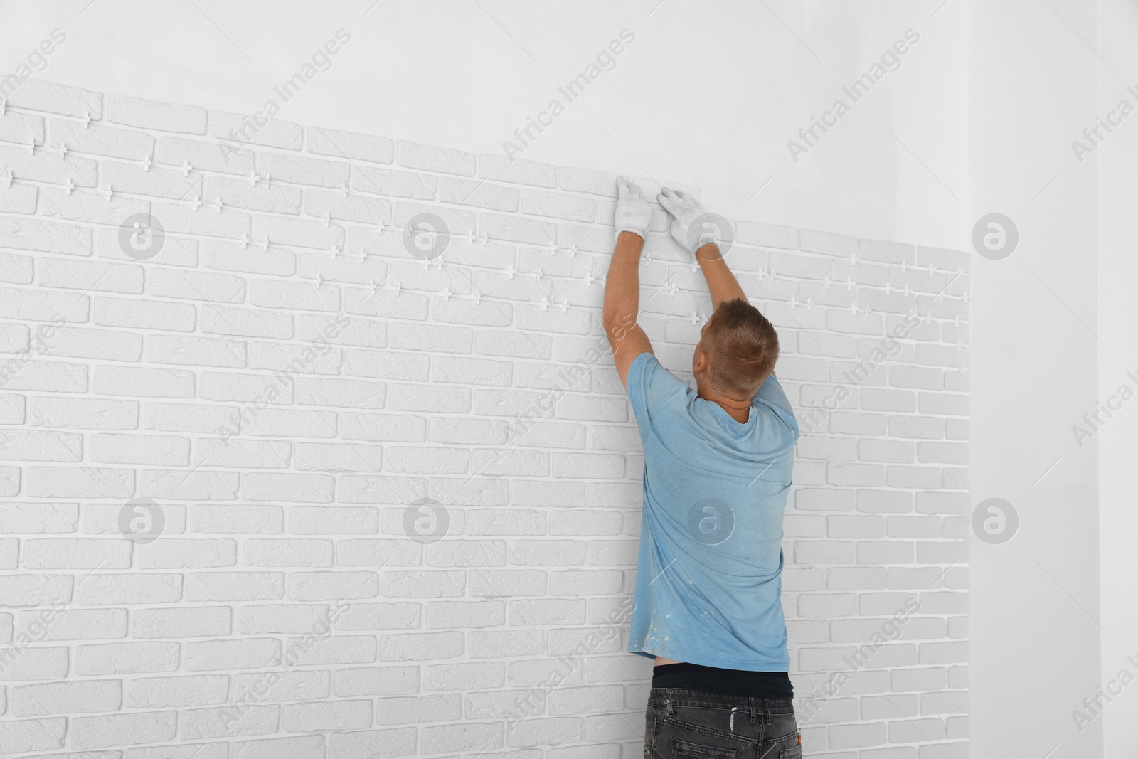 Photo of Professional builder installing new white decorative bricks on wall, back view