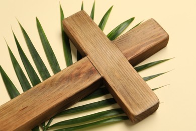 Photo of Wooden cross and palm leaf on beige background, closeup. Easter attributes