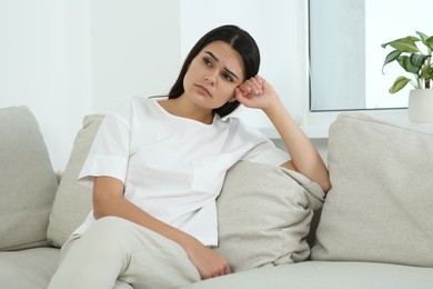 Photo of Depressed young woman sitting on sofa indoors. Hormonal disorders