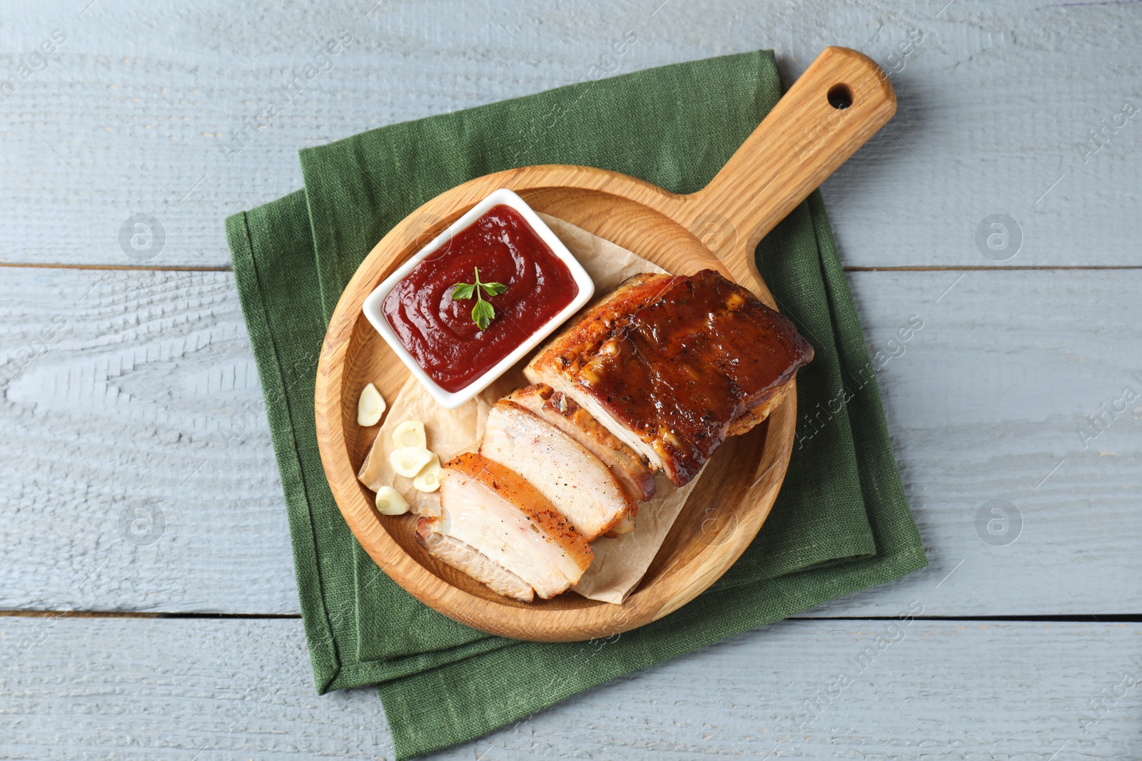 Photo of Pieces of baked pork belly served with sauce on grey wooden table, top view