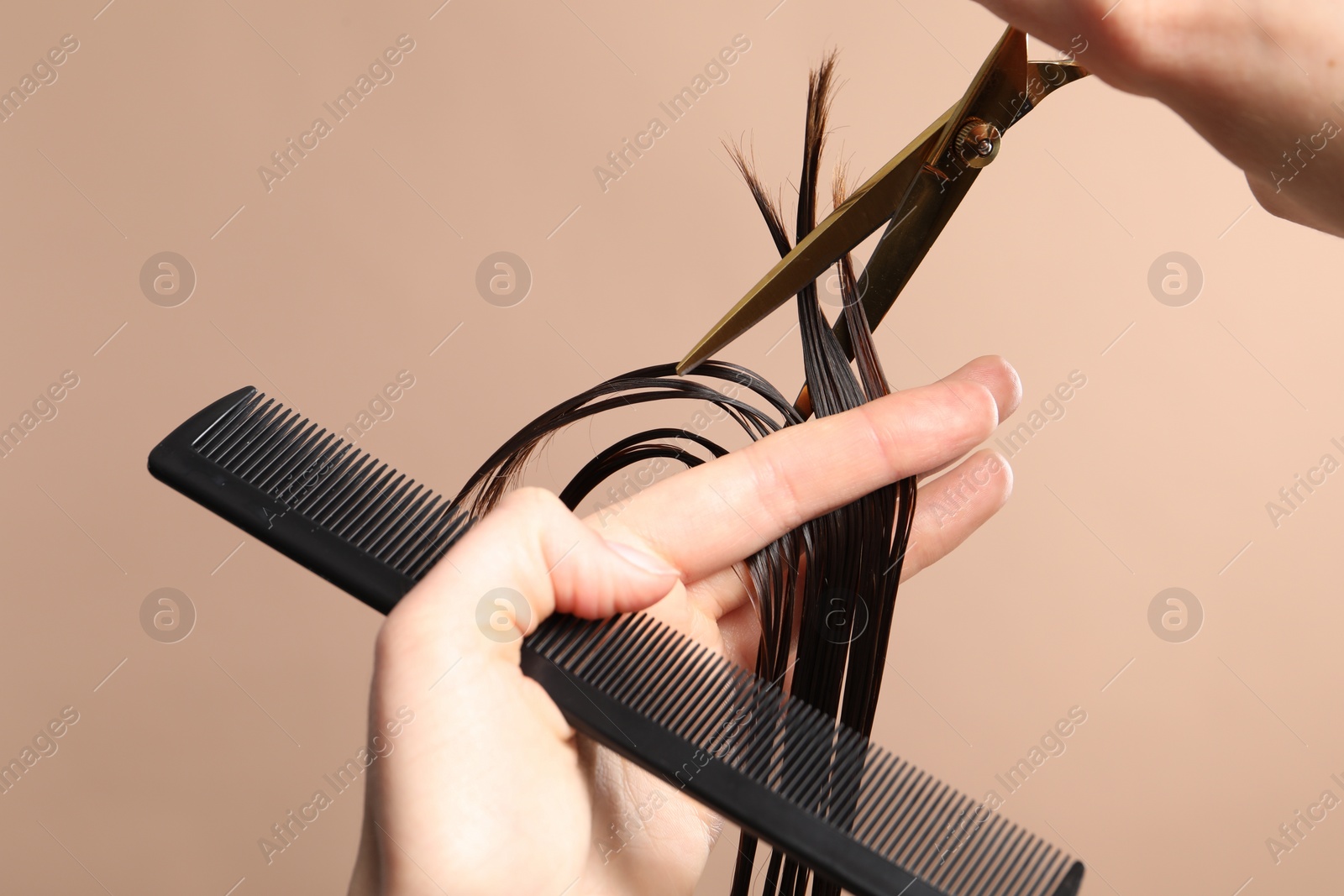 Photo of Hairdresser cutting client's hair with scissors on light brown background, closeup