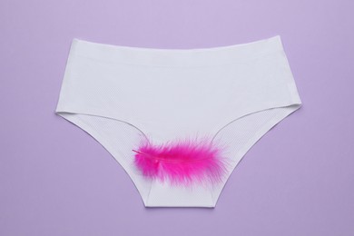 Woman's panties with pink feather on violet background, top view. Menstrual cycle