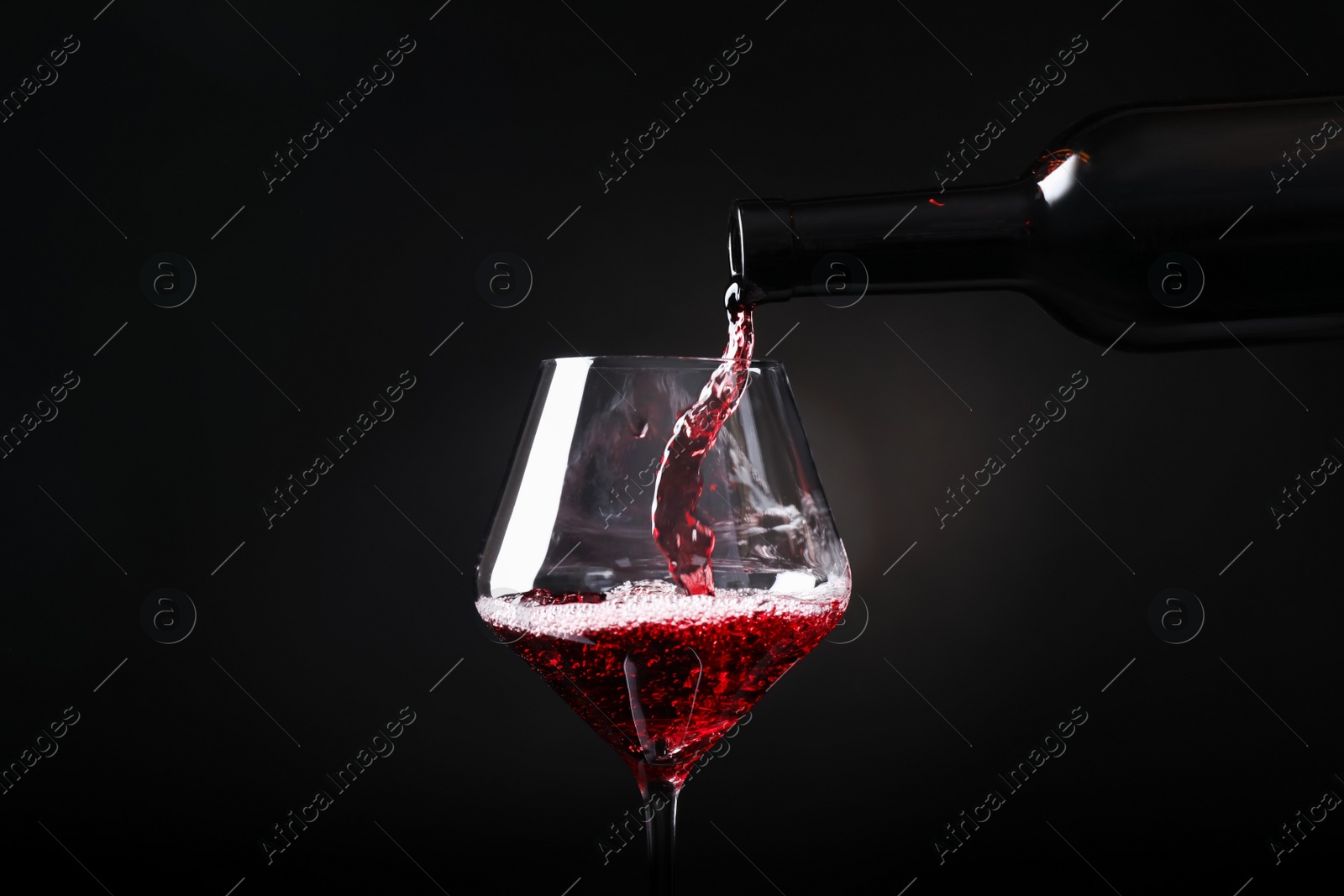 Photo of Pouring red wine from bottle into glass on black background