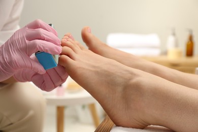 Photo of Professional pedicurist filing client`s toenails in beauty salon, closeup