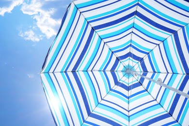 Image of Open big striped beach umbrella and beautiful blue sky with white clouds on background