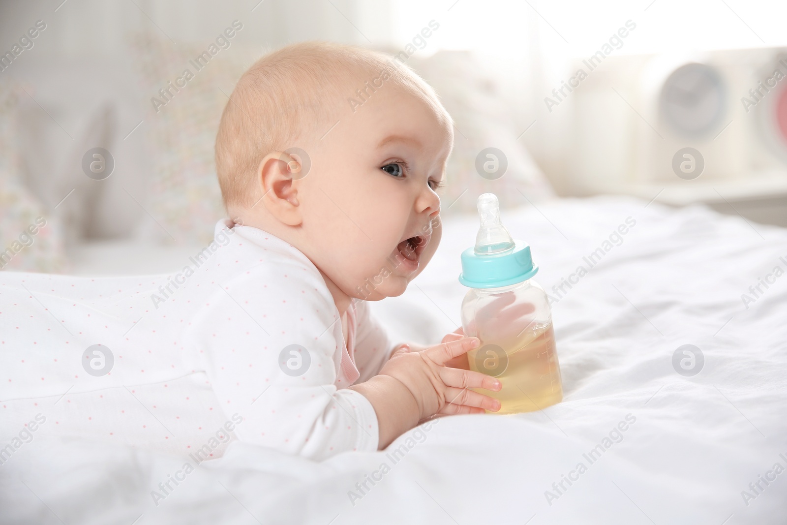 Photo of Pretty baby lying with bottle on bed at home