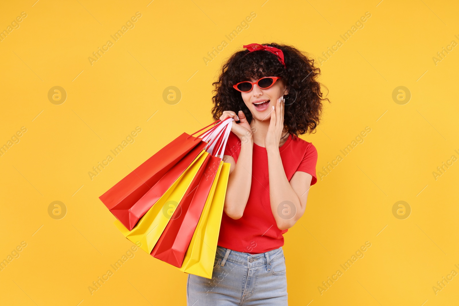 Photo of Happy young woman with shopping bags and stylish sunglasses on yellow background