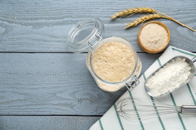 Leaven, flour, whisk and ears of wheat on grey wooden table, flat lay. Space for text