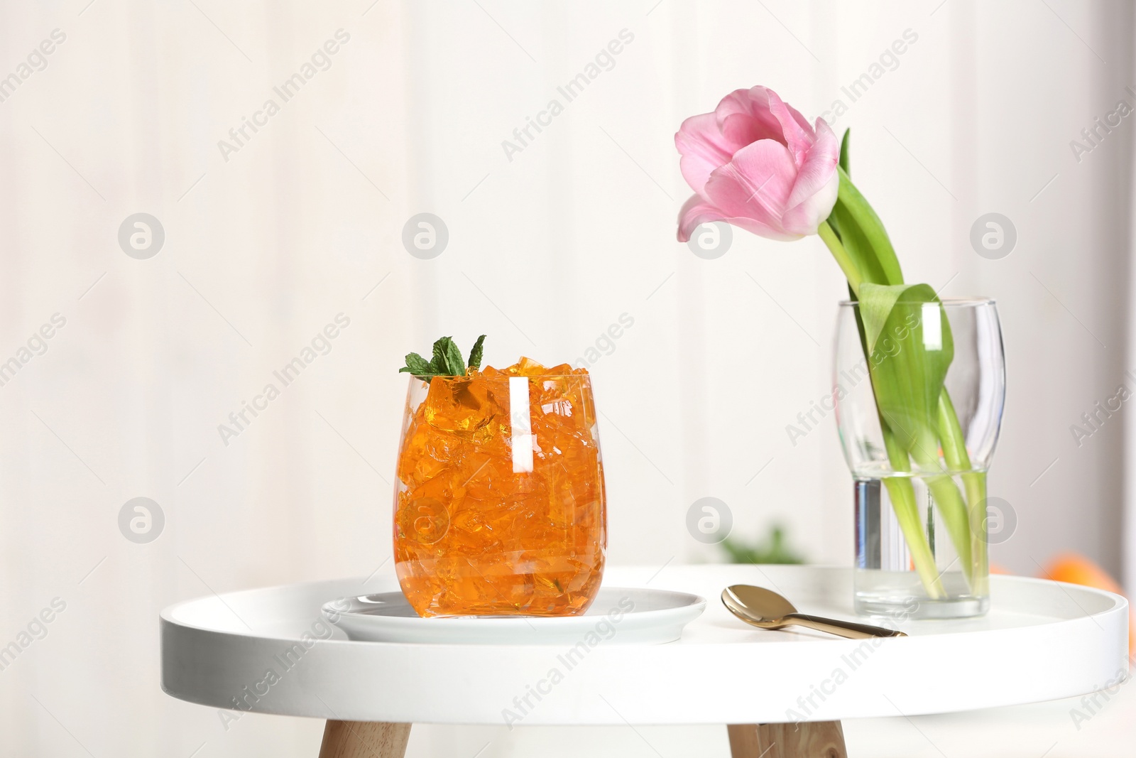 Photo of Glass of jelly and flower on table against blurred background