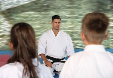 Photo of Children and coach sitting on tatami outdoors. Karate practice