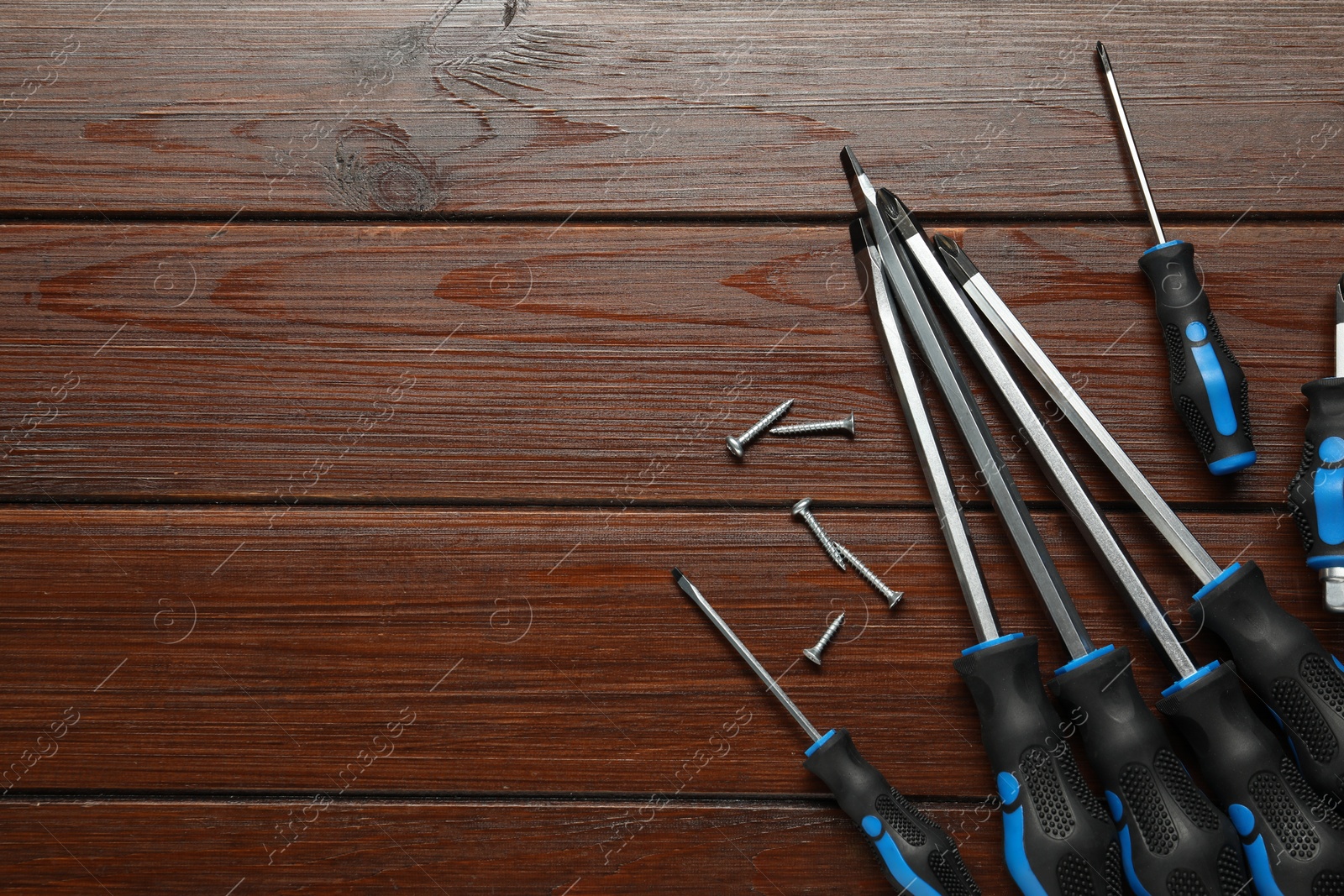 Photo of Set of screwdrivers and screws on wooden table, flat lay. Space for text