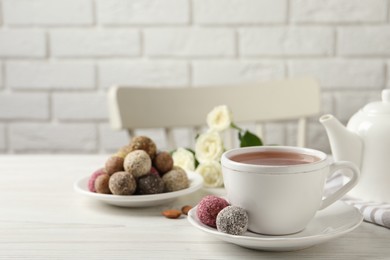 Photo of Cup of aromatic tea and delicious vegan candy balls on white wooden table, space for text