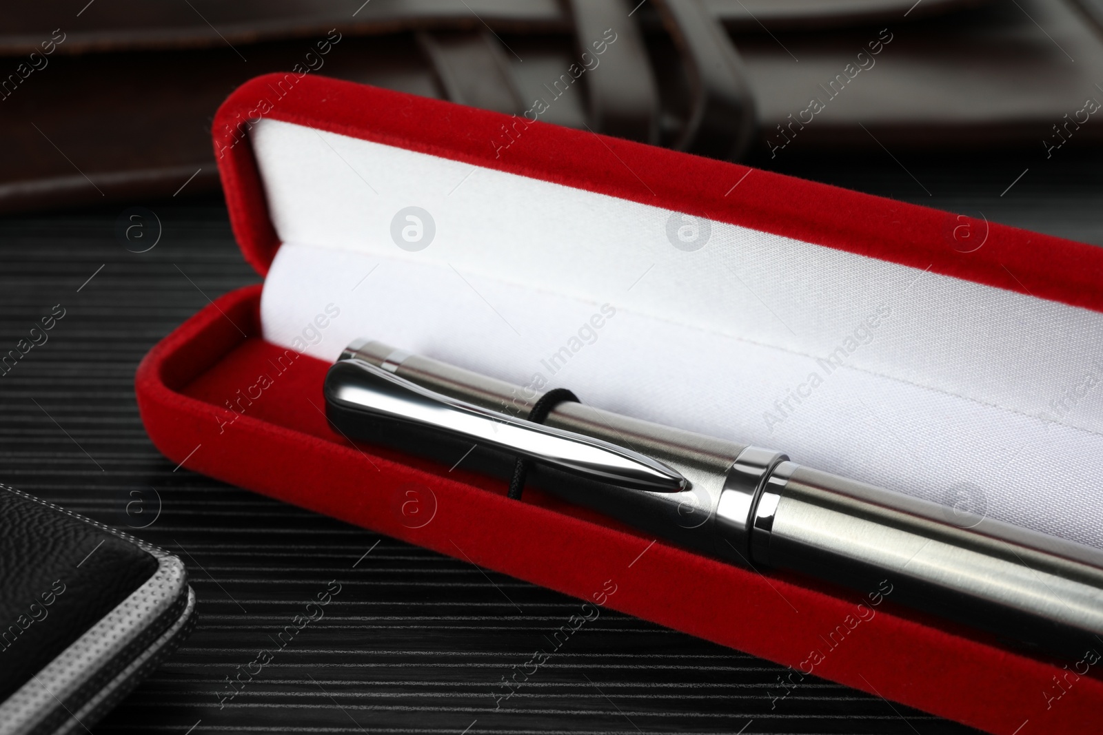 Photo of Case with stylish silver fountain pen and leather notebook on black wooden table, closeup