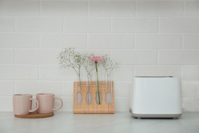 Photo of Modern toaster, cups and flowers on counter in kitchen