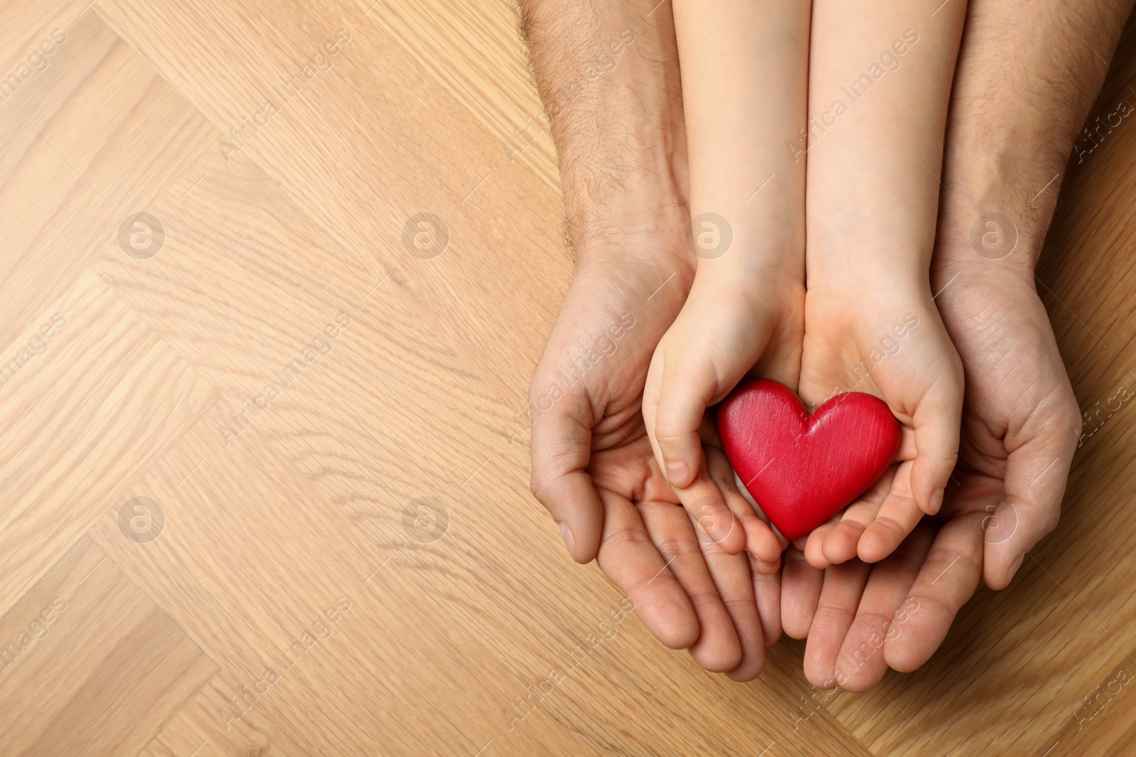 Photo of Man and kid holding red heart in hands at wooden table, top view. Space for text