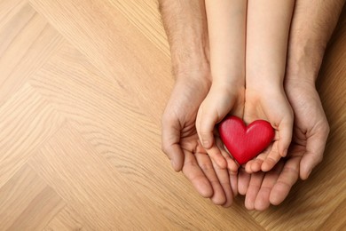 Photo of Man and kid holding red heart in hands at wooden table, top view. Space for text