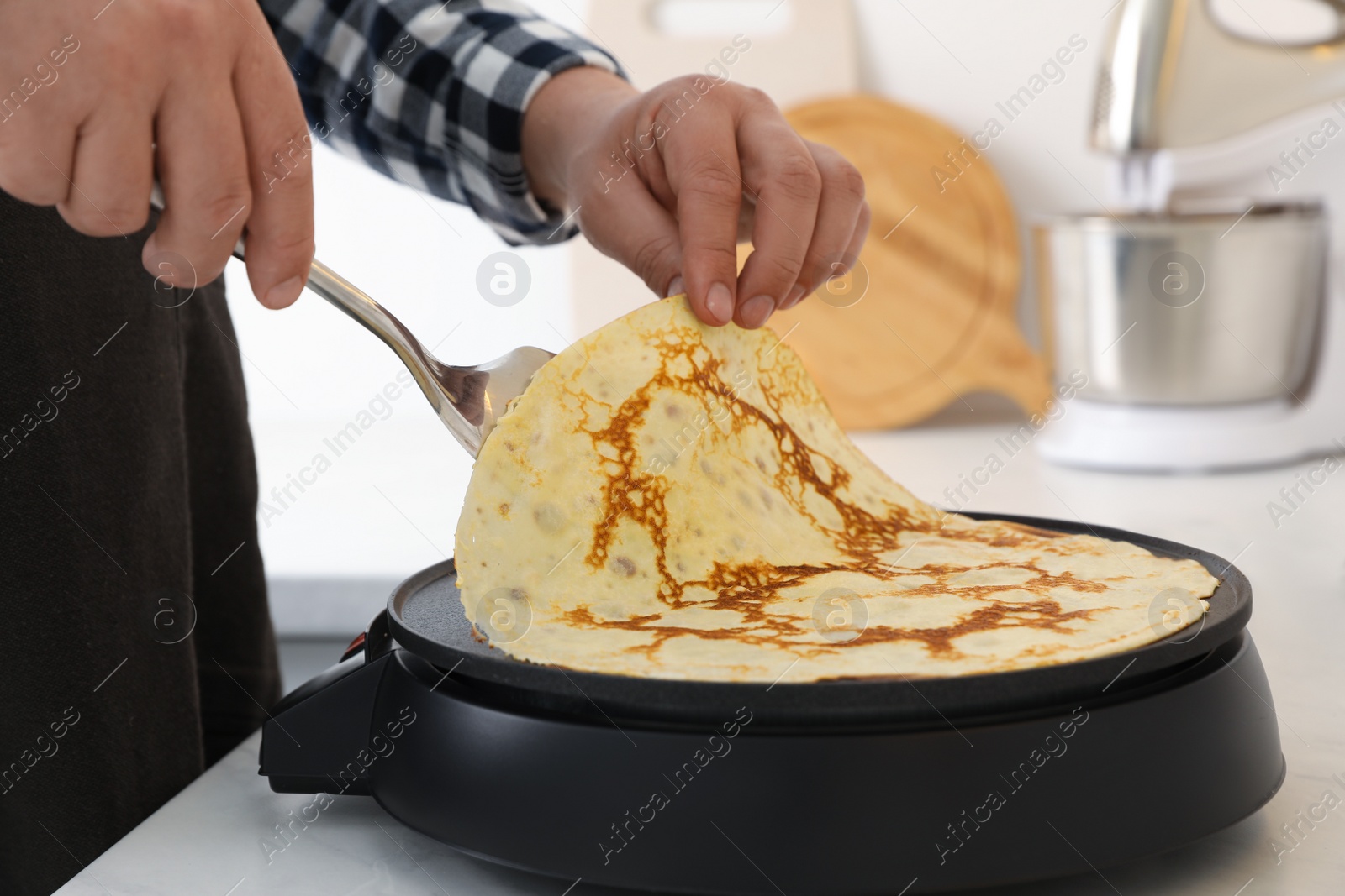 Photo of Man cooking delicious crepe on electric pancake maker in kitchen, closeup