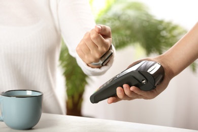 Photo of Woman using terminal for contactless payment with smart watch at table, closeup