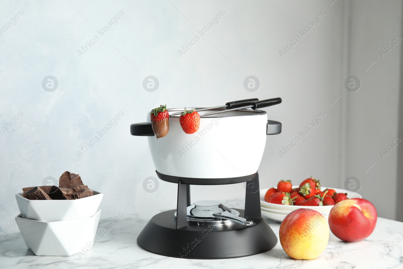 Photo of Chocolate fondue in pot and fresh fruits on marble table