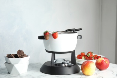 Photo of Chocolate fondue in pot and fresh fruits on marble table