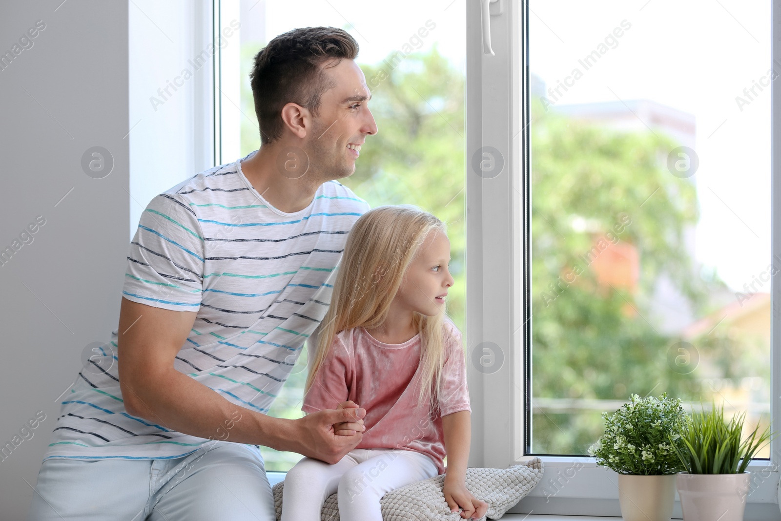 Photo of Young man with cute little girl near window at home