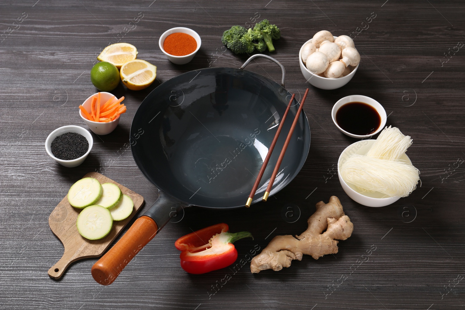 Photo of Empty iron wok and chopsticks surrounded by ingredients on dark grey wooden table