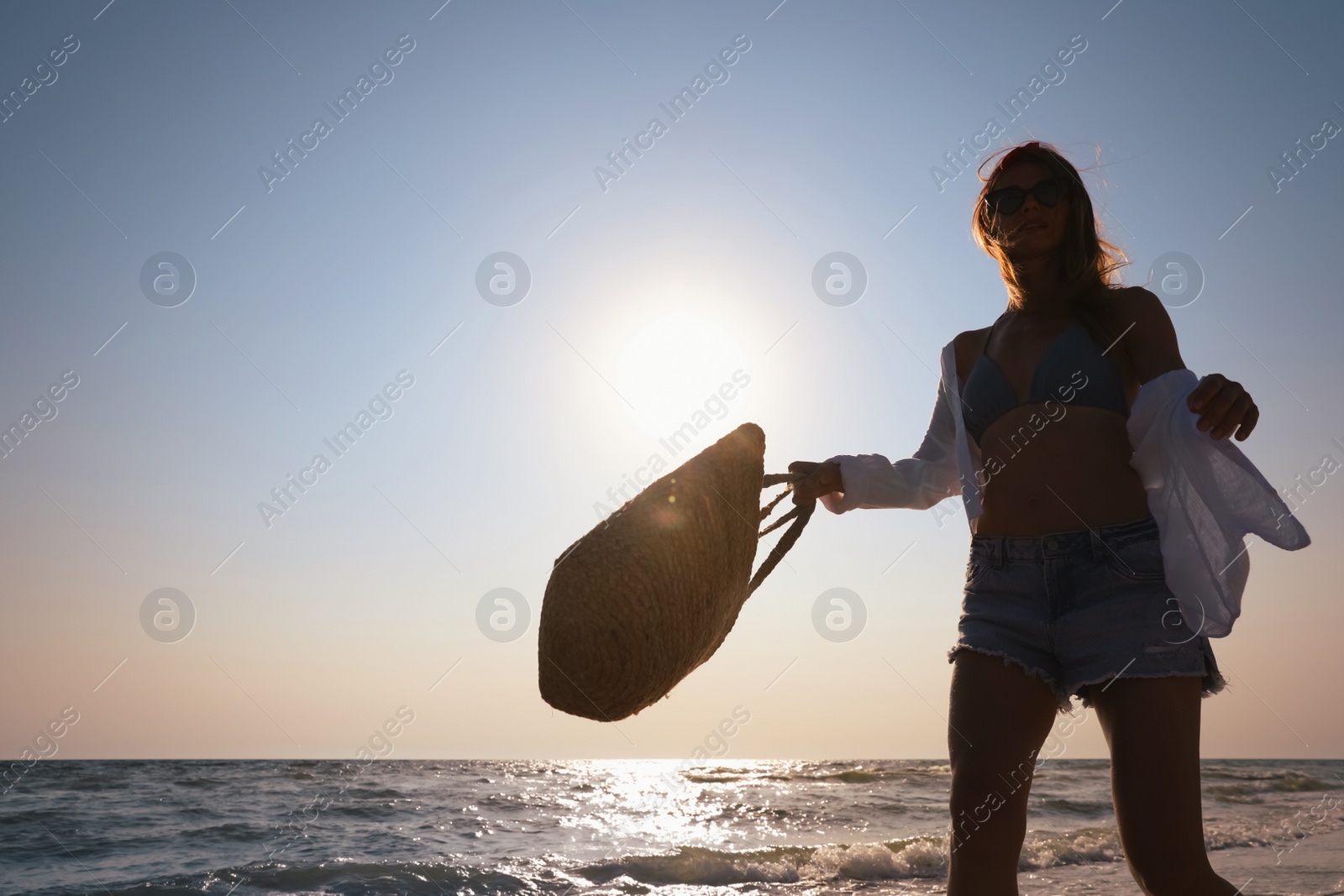 Photo of Woman with beach bag walking on sunlit seashore