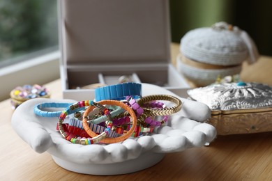 Photo of Ceramic hand stand with many stylish bracelets and jewelry boxes on wooden table, closeup