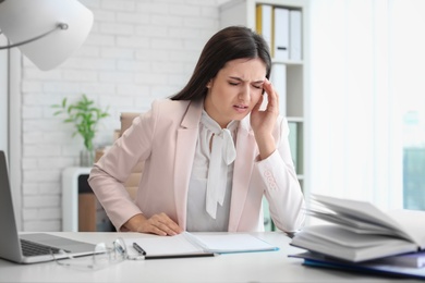 Photo of Young woman suffering from headache while sitting at table in office