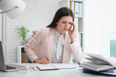 Young woman suffering from headache while sitting at table in office