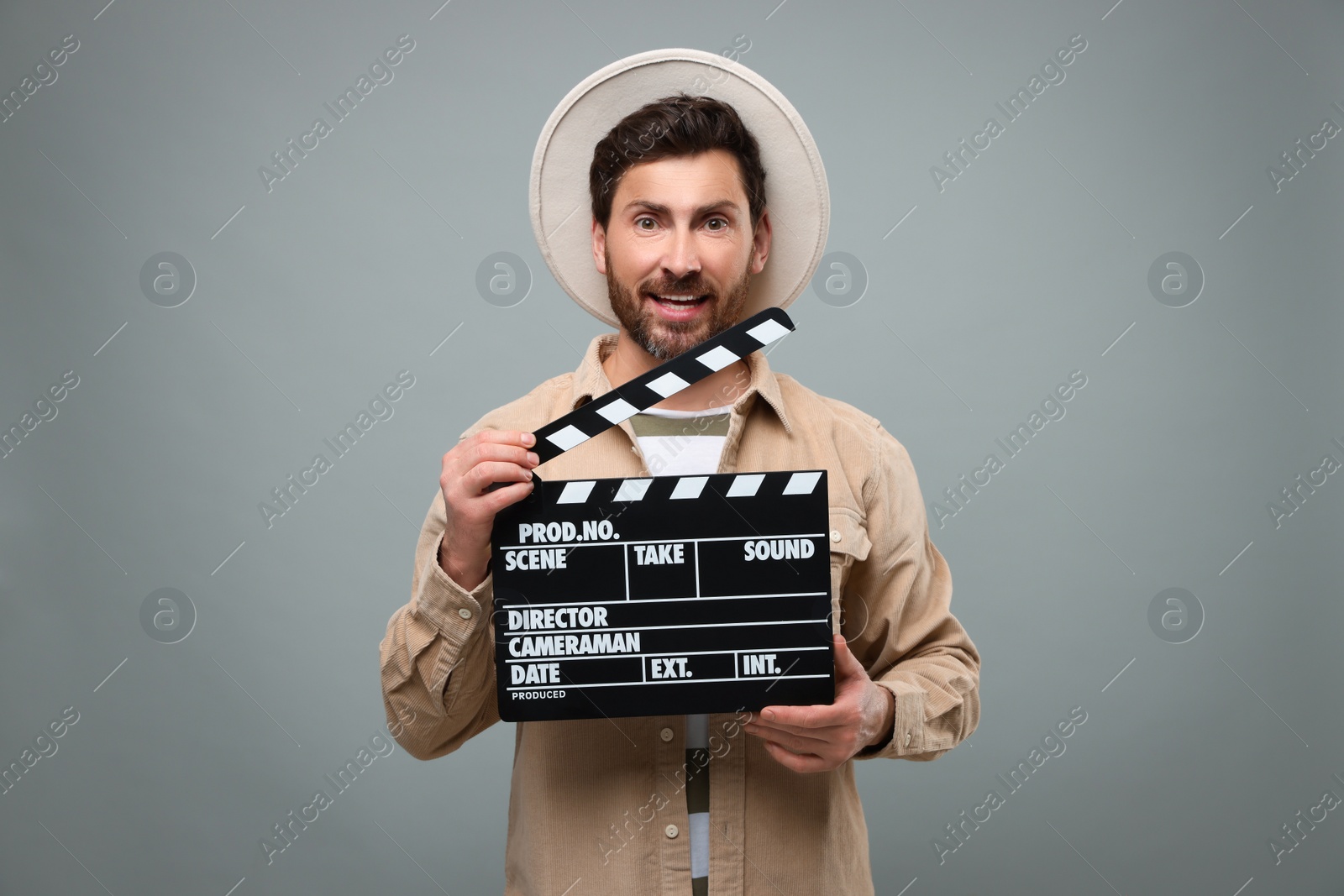 Photo of Smiling actor holding clapperboard on grey background