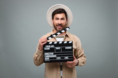 Smiling actor holding clapperboard on grey background