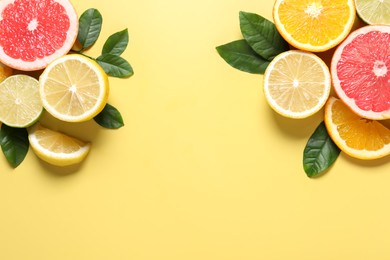 Photo of Different cut citrus fruits and leaves on yellow table, flat lay. Space for text