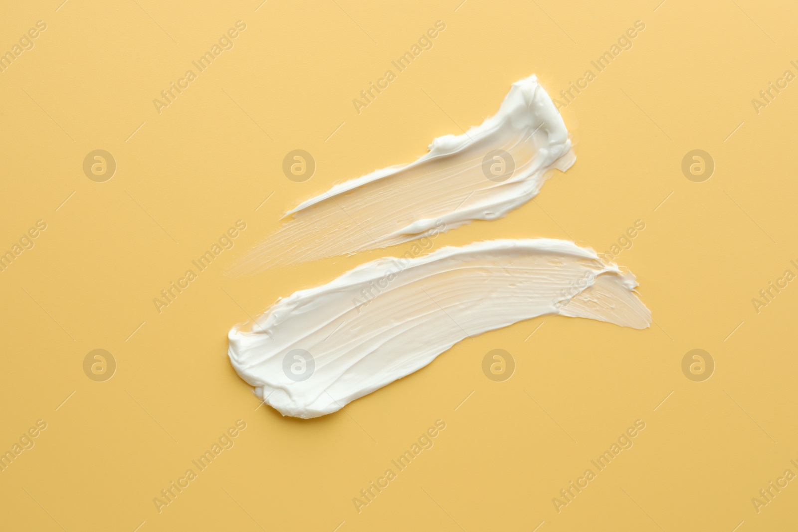 Photo of Samples of face cream on yellow background, top view