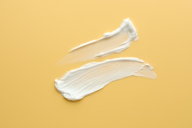 Photo of Samples of face cream on yellow background, top view