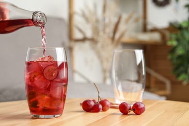 Photo of Pouring grape soda water into glass on wooden table indoors, space for text. Refreshing drink