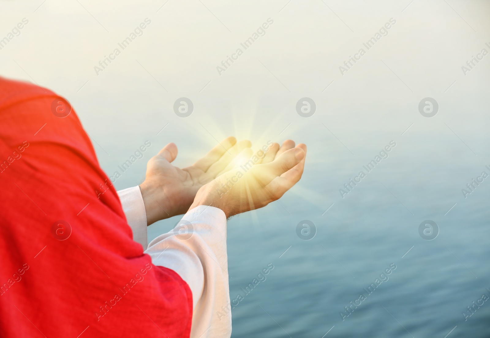 Image of Jesus Christ near water outdoors, closeup. Miracle light in hands
