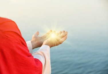 Image of Jesus Christ near water outdoors, closeup. Miracle light in hands
