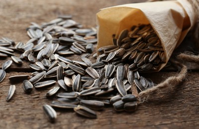 Photo of Overturned paper cone with sunflower seeds on wooden table, closeup