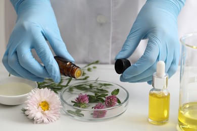 Photo of Scientist developing cosmetic oil at white table, closeup