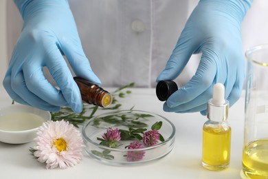 Scientist developing cosmetic oil at white table, closeup