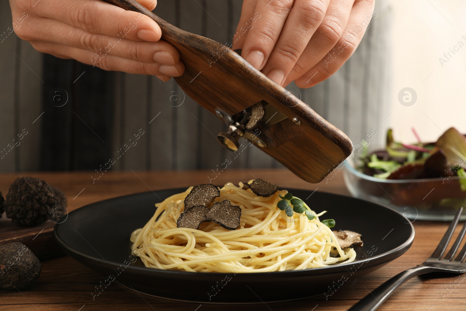 Photo of Woman slicing truffle onto spaghetti at wooden table, closeup