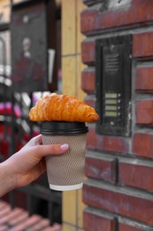 Photo of Woman holding croissant and paper cup in hand outdoors, closeup