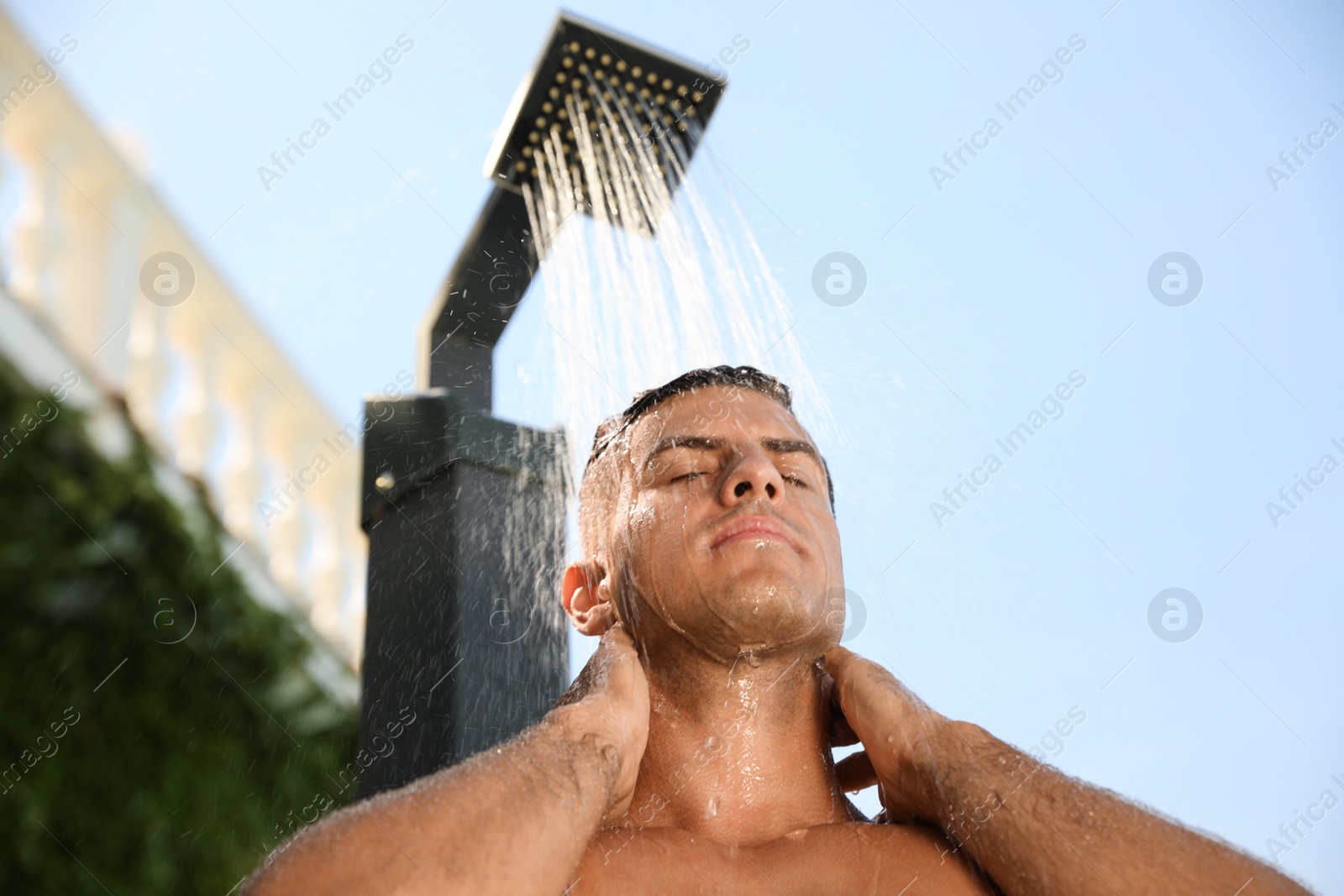 Photo of Man washing hair in outdoor shower on summer day