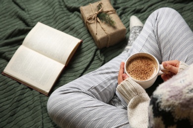 Photo of Woman in knitted socks sitting on warm plaid with hot cocoa, closeup
