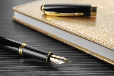 Stylish fountain pen and notebook on black wooden table, closeup