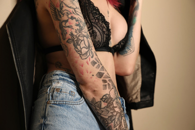 Beautiful woman with tattoos on body against beige background, closeup