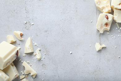 Pieces of white chocolate with nuts on light grey table, flat lay. Space for text