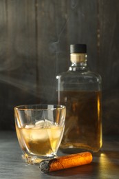 Photo of Bottle, glass of whiskey with ice cubes and smoldering cigar on black wooden table